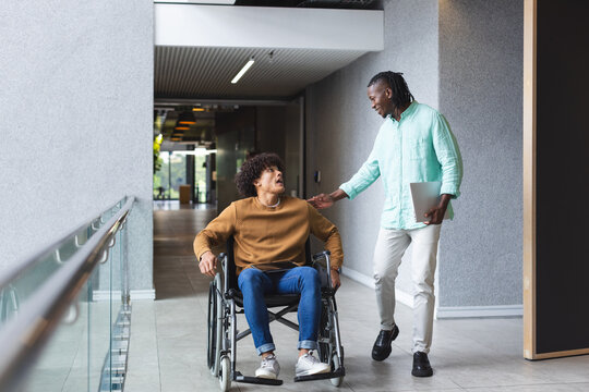 African American man walks beside smiling biracial man in wheelchair in a business office - Powered by Adobe
