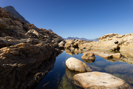 Rugged rocks surround calm water reflecting blue sky, copy space