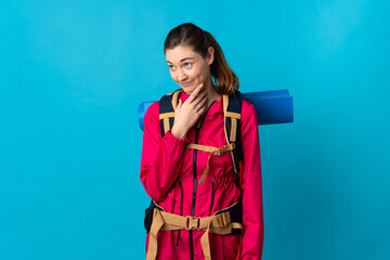 Young mountaineer woman over isolated blue background looking up while smiling