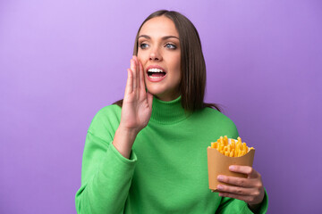 Young caucasian woman holding fried chips on purple background shouting with mouth wide open to the side