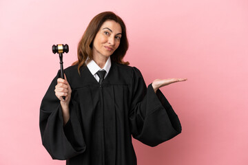 Middle aged judge woman isolated on pink background extending hands to the side for inviting to come