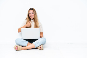 Naklejka premium Young woman with laptop sitting on the floor isolated on white background giving a thumbs up gesture