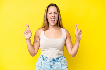 Young caucasian woman isolated on yellow background with fingers crossing