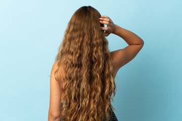 Young blonde woman isolated on blue background in back position and thinking