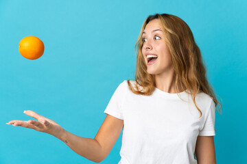 Young blonde woman isolated on blue background holding an orange