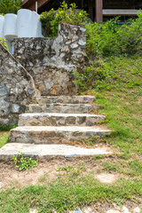 A staircase with steps made of stones filled with mortar leading up the green lawn and grass.