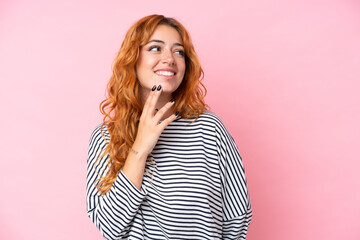 Young caucasian woman isolated on pink background looking up while smiling