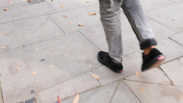 Urban stroll in London, male with black sneakers, grey pants slowly walking amidst autumn leaves