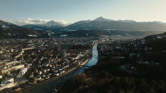Aerial drone shot of city of Innsbruck, Tyrol, Austria. Cityscape view during golden hour sunset, snow covered mountains in distance