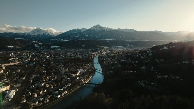 Aerial drone: city of Innsbruck, Tyrol, Austria. Cityscape view, houses, town, river and snow covered mountains, golden hour