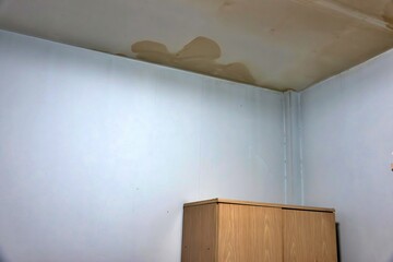 A corner of a room with a brown stain on the ceiling. The stain is likely from a leak or water...