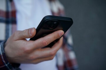 A man in a white T-shirt and shirt holds a phone in his hands