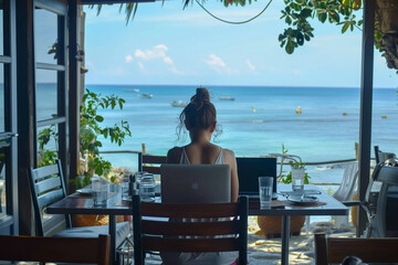 Woman with laptop, overlooking the ocean from a restaurant table.