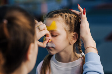 A woman professional artist paints with a brush, a colored pencil on the face of a child, a beautiful girl, face painting, makeup, drawing. Photography, creative process.