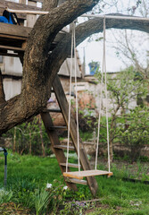 A homemade swing for children hangs on a rope on a tree in an outdoor garden.