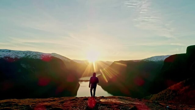 Man Walks towards the sunset skyline mountain range lake drone shot from behind