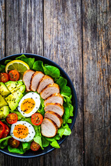 Tasty salad - roasted veal loin, avocado, boiled eggs and fresh vegetables on wooden table
