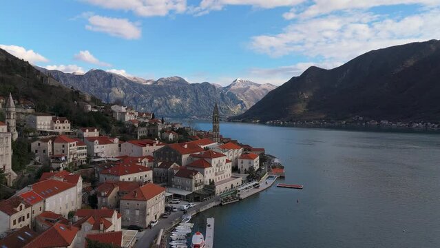 4K drone shot captures the charming town of Perast, Montenegro, with a beautiful view of Saint Nicholas Church, the UNESCO-listed Bay of Kotor, and mountains in the background