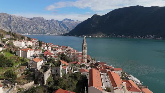 4K drone footage captures Saint Nicholas Church in the charming town of Perast, Montenegro, with a beautiful view of the UNESCO-listed turquoise Bay of Kotor and mountains in the background