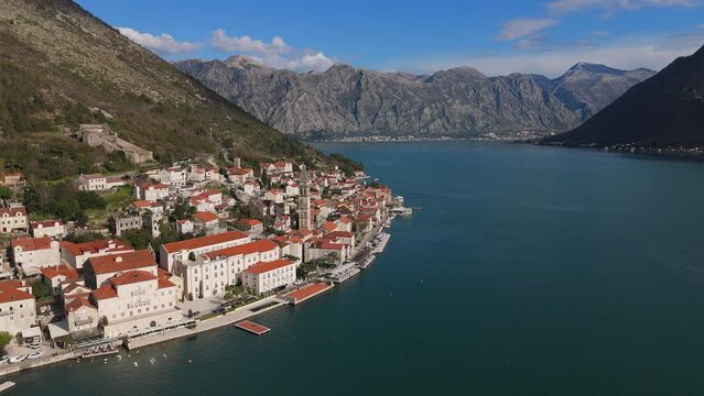 4K drone footage captures Saint Nicholas Church in the charming town of Perast, Montenegro, with a beautiful view of the UNESCO-listed turquoise Bay of Kotor and mountains in the background