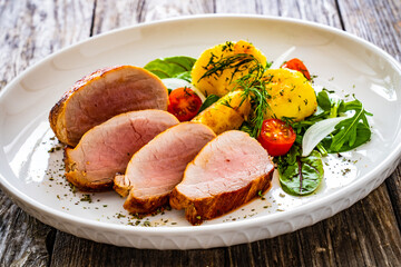 Fried pork loin with boiled potatoes and fresh vegetables on wooden table
