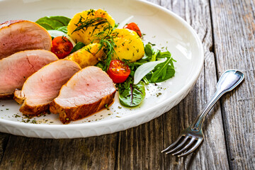 Fried pork loin with boiled potatoes and fresh vegetables on wooden table
