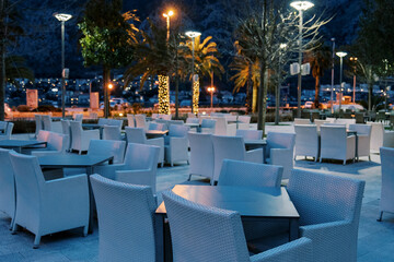 Wicker chairs stand around tables in an open-air restaurant under the light of lanterns
