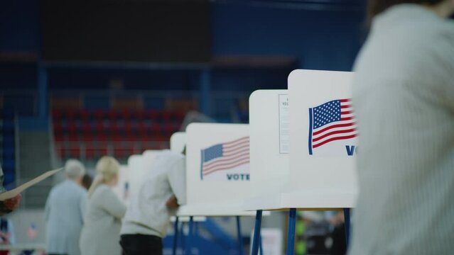 Elderly male voter with bulletin in hands comes to voting booth. Multicultural American citizens come to vote in polling station. Political races of US presidential candidates. National Election Day.