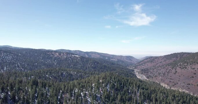 Aerial view of a New Mexico mountain valley flies back to reveal a rural highway