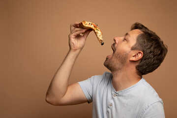 Studio portrait of a man in his 40s wearing a blue shirt and eating a piece of pizza. There is...
