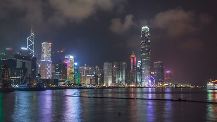 Hong Kong city skyline at night over Victoria Harbor with cloudy sky and urban skyscrapers timelapse hyperlapse.