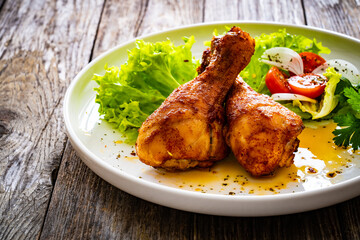 Roast chicken drumsticks with lettuce and tomatoes on wooden table
