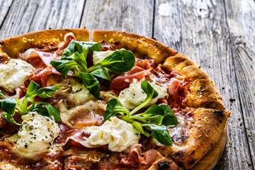 Circle prosciutto pizza with mascarpone cheese, ripening ham and leafy greens on wooden table
