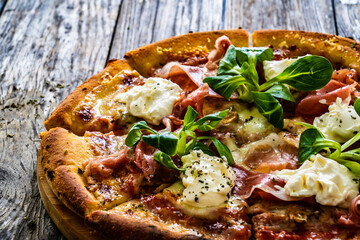 Circle prosciutto pizza with mascarpone cheese and leafy greens on wooden table
