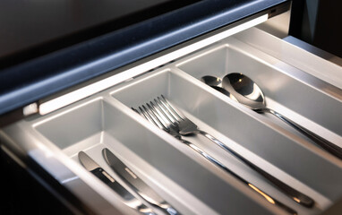 Close-up photo of cutlery in modern illuminated kitchen drawer