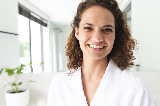 Caucasian young woman wearing white robe, smiling in bathroom