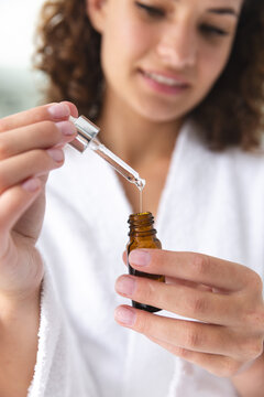 A young Caucasian woman at home holding dropper and bottle, focusing on liquid