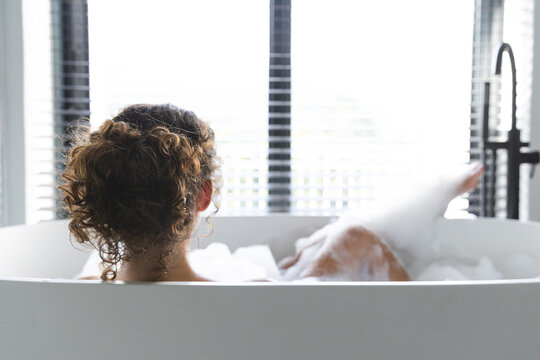 A young Caucasian woman relaxing at home in bathtub, enjoying alone time, copy space