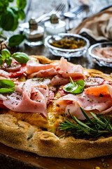 Pinsa Romana with cooked ham, mozzarella and vegetables on wooden table
