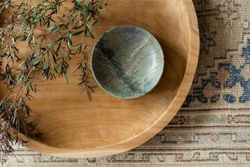 Green marble bowl on wooden tray with foliage and turkish rug