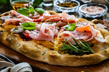 Pinsa Romana with cooked ham, mozzarella and vegetables on wooden table
