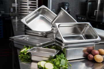 Stacked stainless steel pans and fresh vegetables on prep table