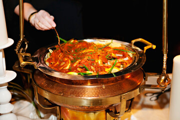 Chef serves gourmet pasta from a steaming chafing dish.