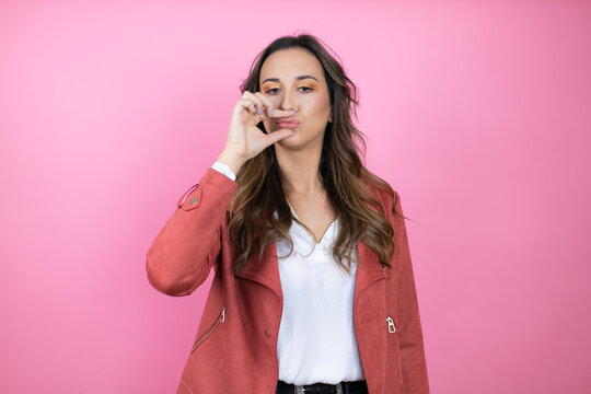Young beautiful woman wearing casual jacket over isolated pink background mouth and lips shut as zip with fingers. Secret and silent, taboo talking