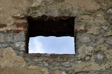 View of blue sky through square window of loophole in wall of an ancient fortress. Copy space. Selective focus.