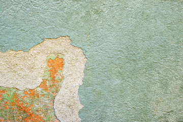 Colorful green-orange-yellow wall surface of an old building with crumbling plaster and stains as a textured background. Copy space. Selective focus.