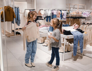 Two Young Girls Trying on Clothes in a Brightly Lit Clothing Store