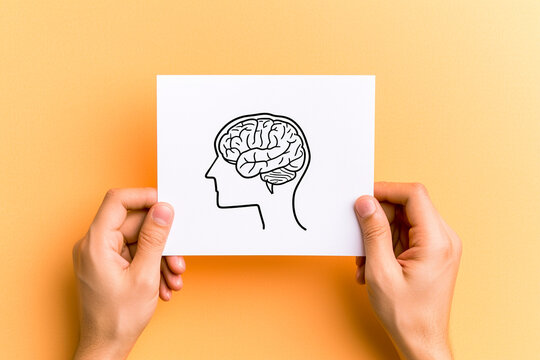 Hands holding white paper with human head and brain on yellow background. Mental health and positive thinking concept