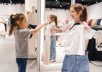 Two Young Girls Trying Clothing in a Bright Retail Store During Shopping Day