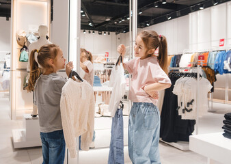 Little girls choose clothes in the store. Kids shopping at the mall.